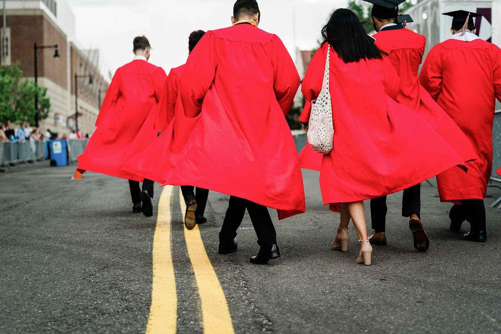 6 graduating seniors wearing their grad caps and gowns walk towards the BU Commencement ceremony for undergrads, their red robes flowing out behind them.