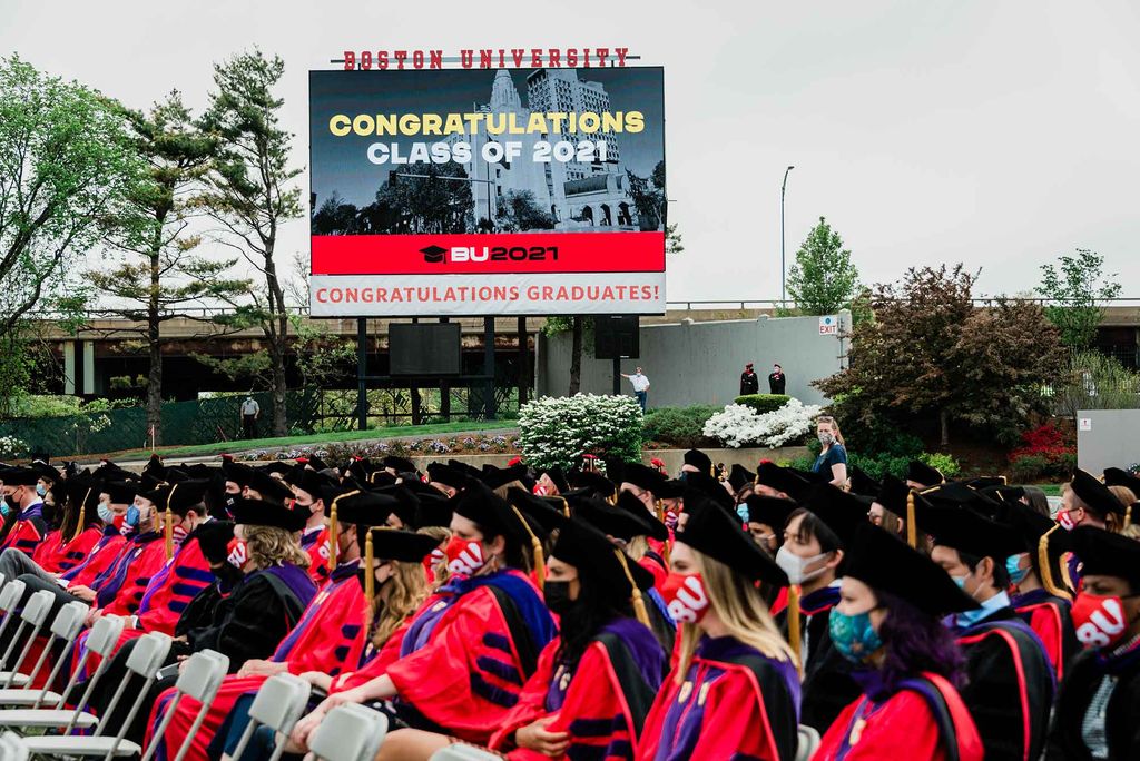 A view of the Nickerson Field digital scoreboard across several rows of seated graduates. The message on the scoreboard reads 'Congratulations Class of 2021. BU2021. Congratulations Graduates!'