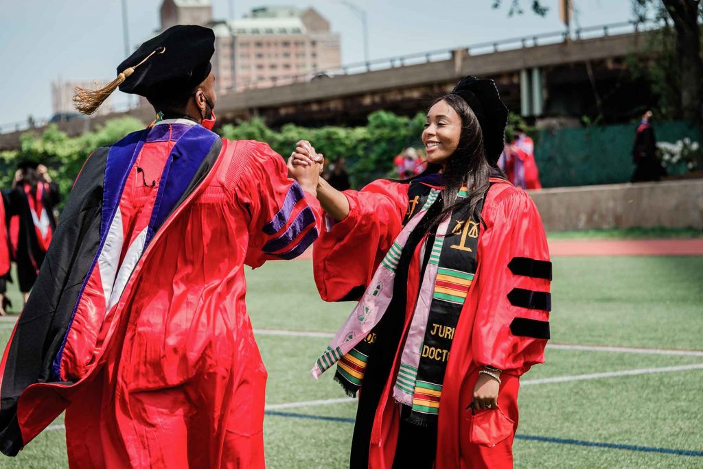 Two African American students share a celebratory handshake following the advanced degrees ceremony at Boston University's 148th Commencement