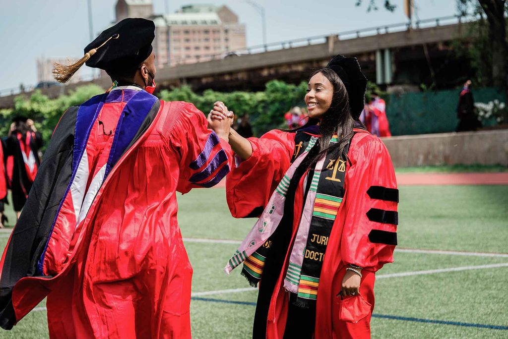 Two African American students share a celebratory handshake following the advanced degrees ceremony at Boston University's 148th Commencement