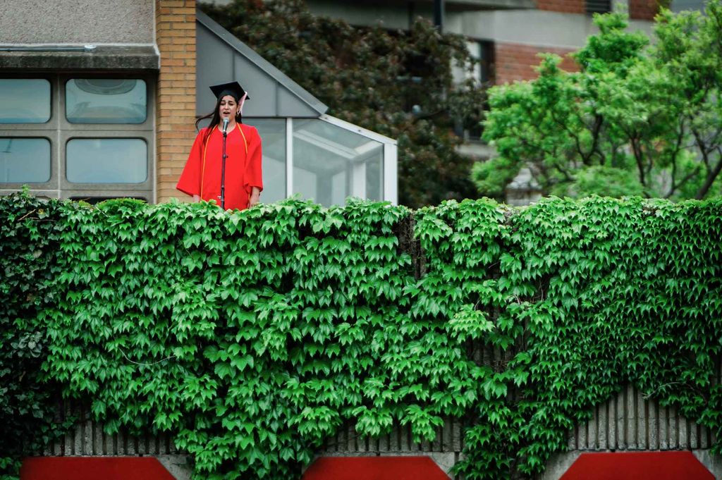 The BU Commencement student singer performs from a perch covered with ivy overlooking Nickerson Field during the undergraduate degree ceremony.