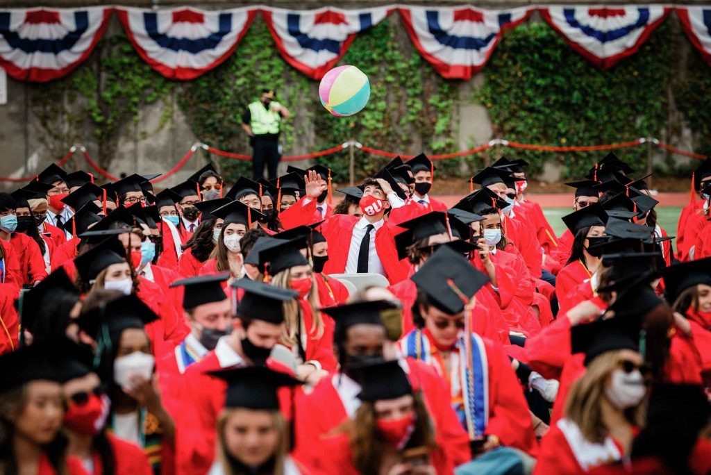A graduating student hits a beach ball up into the air among a section of many graduates during the 2021 BU Commencement.