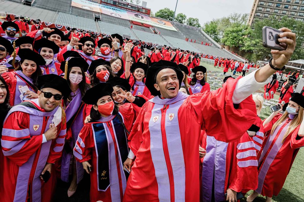 A group of graduate students in red gowns with bright purple adornments pose for a selfie following the 2021 BU Commencement ceremony for advanced degrees.