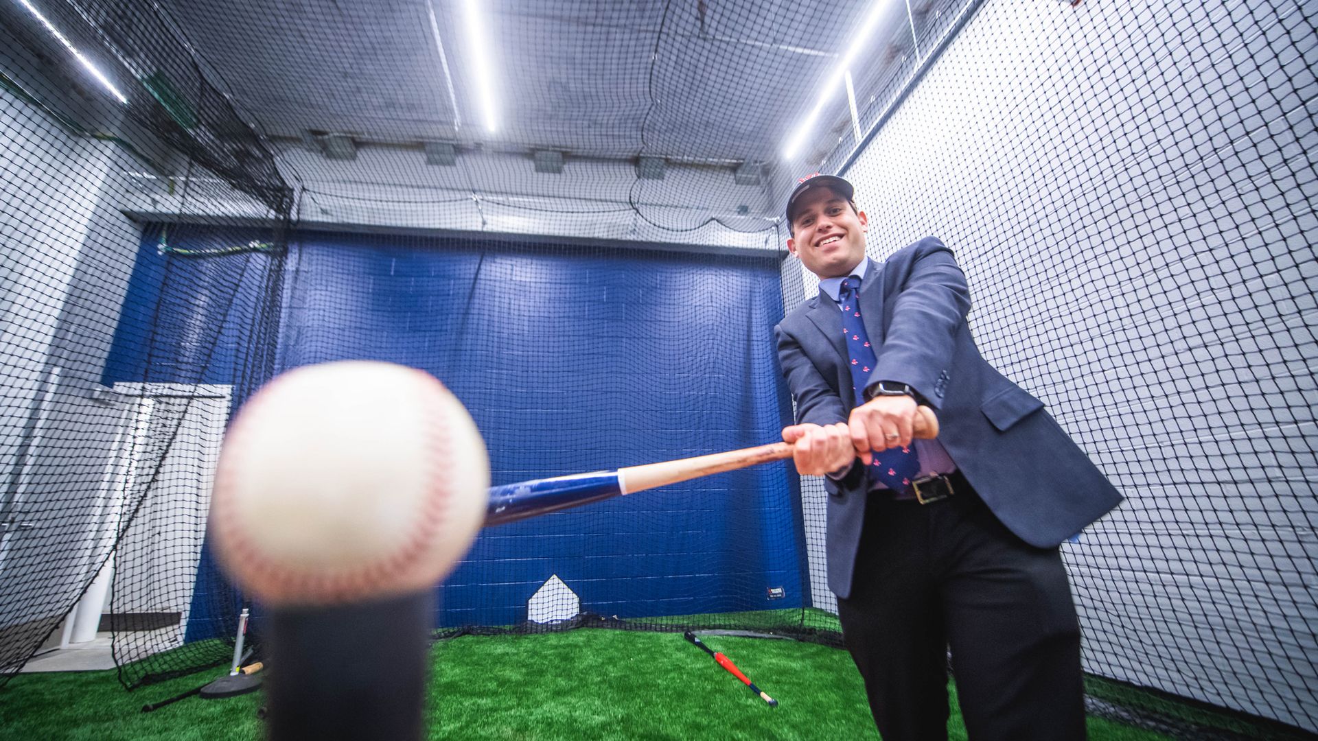 Matt Levin in the batting cages at the Worcester Red Sox stadium. He is holding a bat and swinging at a ball on a tee.