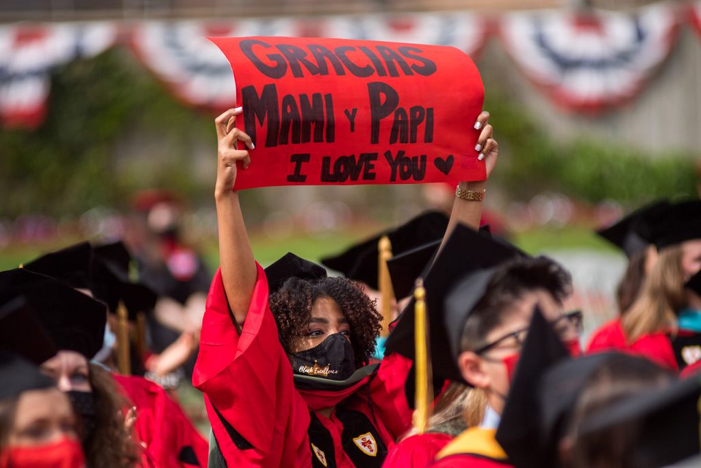 A graduate holding up a sign reading "Thank You Mami and Papi"