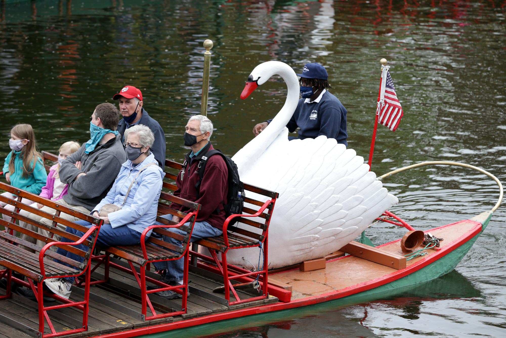 A photo of Swan Boats in Boston Public Garden. Passengers on the boats are wearing masks.