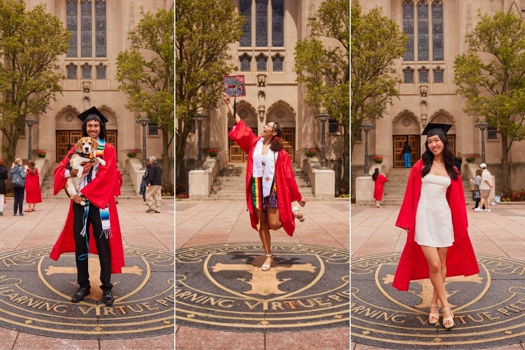 Photo: Three Boston University graduates in red gowns stand on the Boston University seal on the ground. The first graduate holds a dog, the second raises a decorated cap, and the third poses with hands on hips. All are in front of a large building with arched windows and trees.