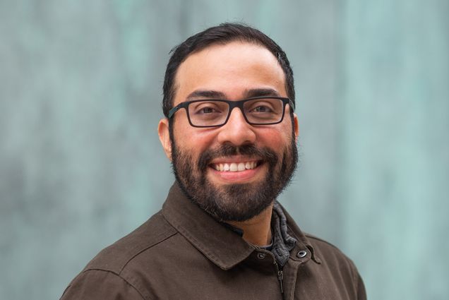 Headshot of Steve Ramirez, a CAS assistant professor of psychological and brain sciences, smiling in a brown button down, as he stands in front of a blue wall. He wears black glasses.