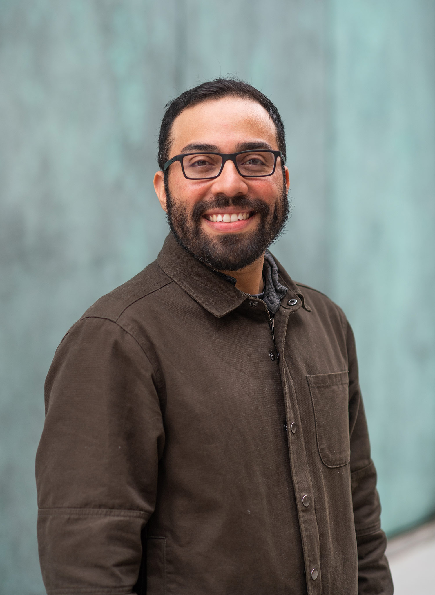 Headshot of Steve Ramirez, a CAS assistant professor of psychological and brain sciences, smiling in a brown button down, as he stands in front of a blue wall. He wears black glasses.