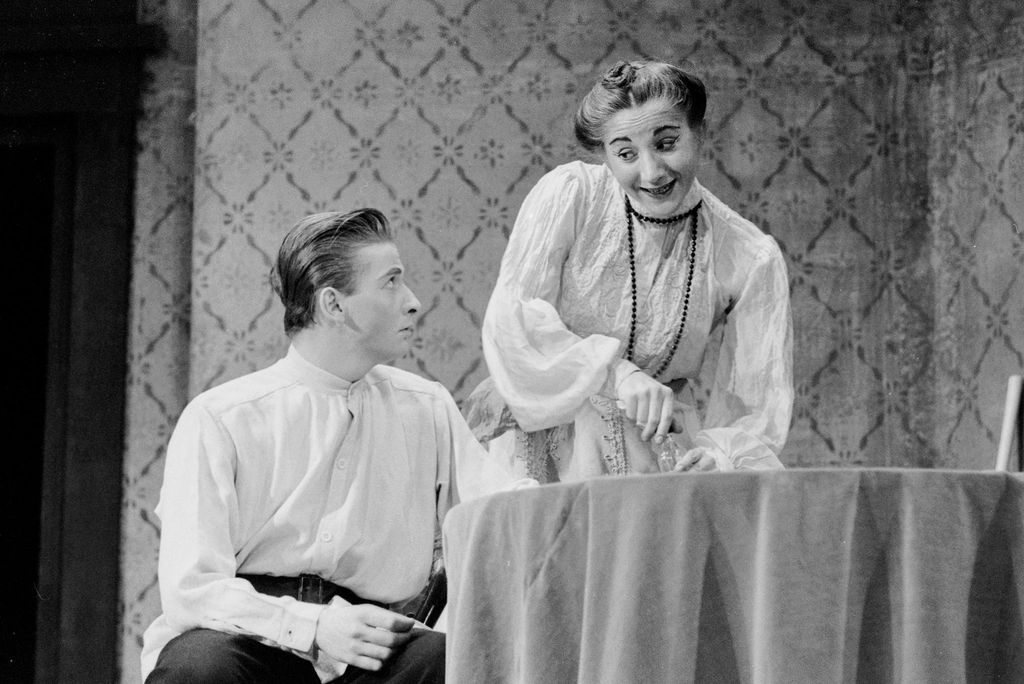 Black and white photo of Olympia Dukakis as Irina Nicolayevna Arcadina, Madame Trepleff at the Boston University Theatre in a student production of "The Seagull" from 1957. Dukakis is heavily made up and wears a flowy white gown and has her hair in a bun.