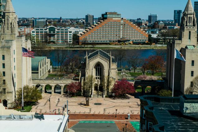 Drone shot of Marsh Chapel, Marsh Plaza, with hotel across the Charles River in the background. The plaza and street out front is empty.