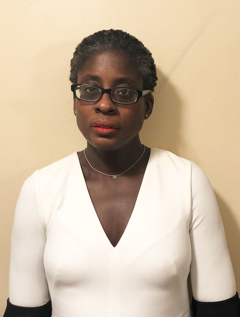 Photo of Ridianee Denis in a white blouse; she wears glasses and looks concentratedly at the camera.