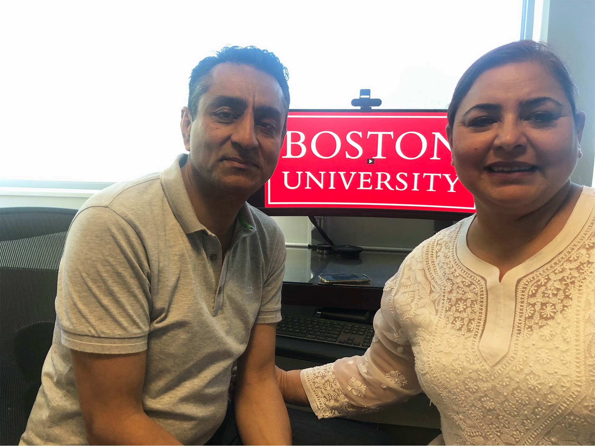 Neal and Shireen Singh pose for a photo in front of the BU Commencement Ceremony livestream playing on their computer.
