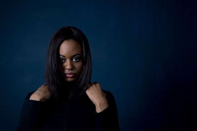 A photo of a woman with her hands on her shoulders against a navy blue background