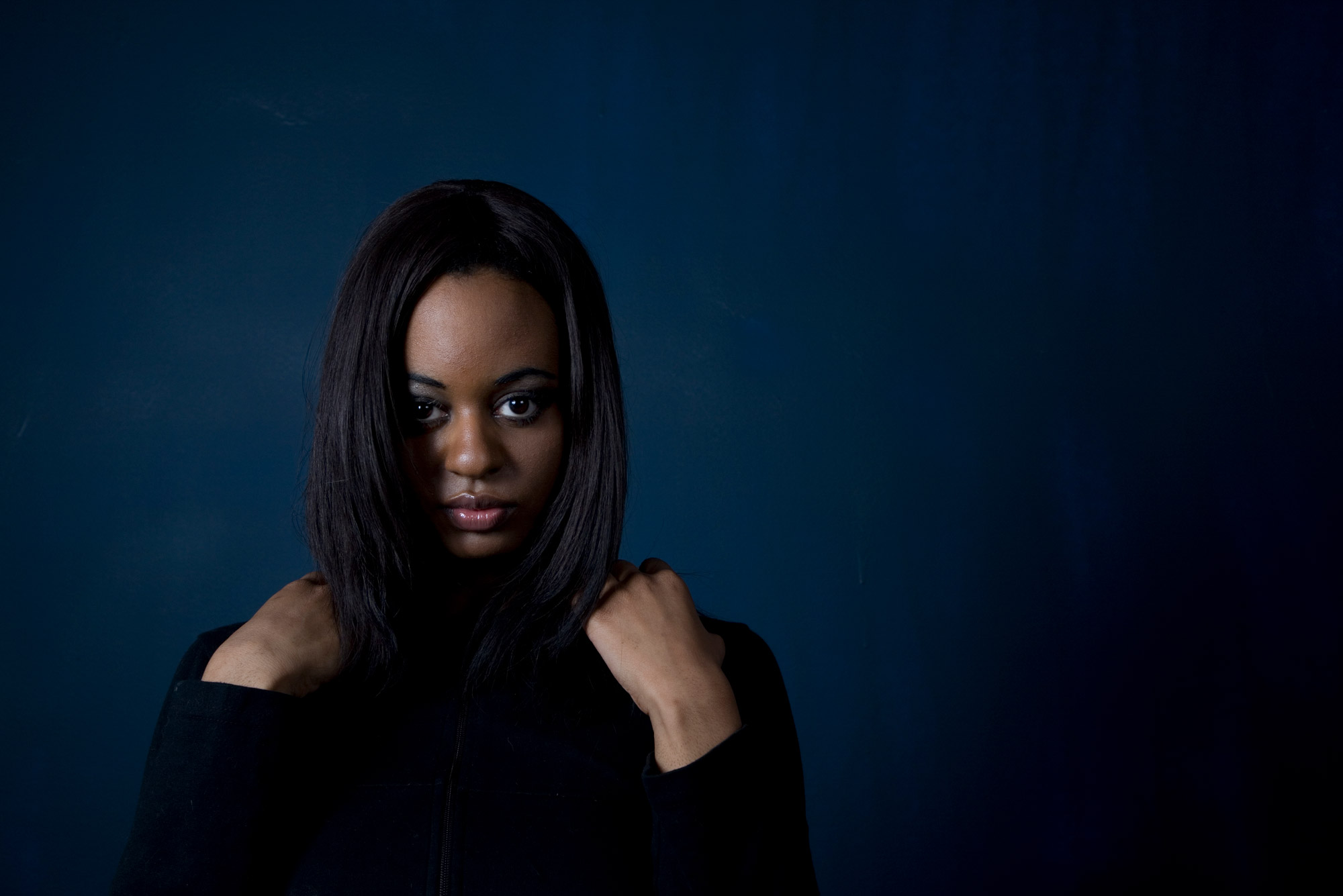 A photo of a woman with her hands on her shoulders against a navy blue background