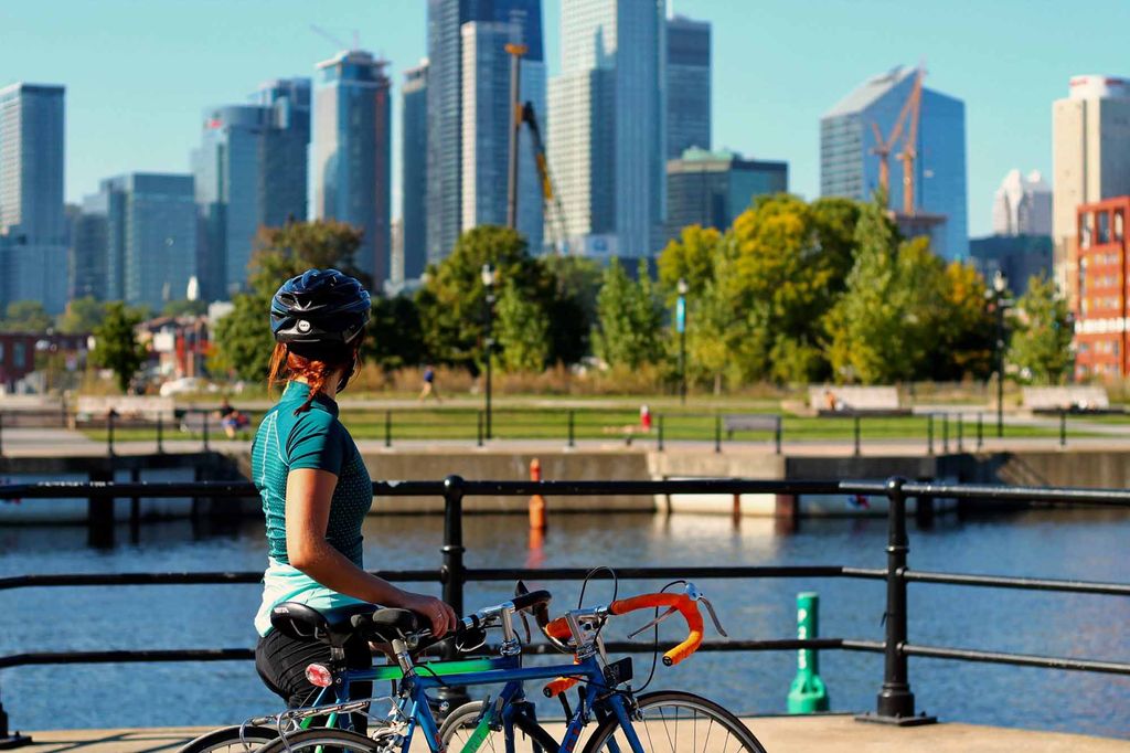 A woman cyclist standing next to her bike looks at the Montreal skyline from a city park.