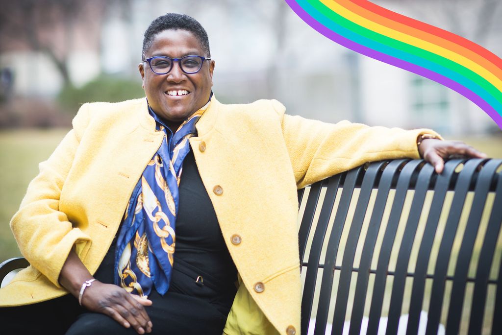 Photo of Judi Burgess, BU’s director of labor relations, in a yellow blazer, and blue and gold scarf, sitting on a bench and smiling. A rainbows is overlaid on the top right.