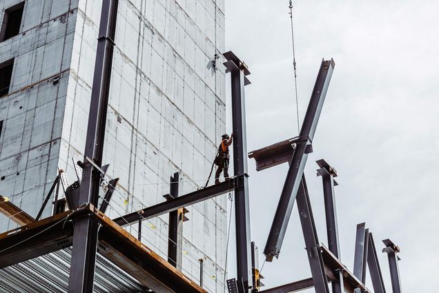 Photo of a construction worker standing on the large steel beam scaffolding of the future Center for Computing & Data Sciences building. The sky behind them is light blue.