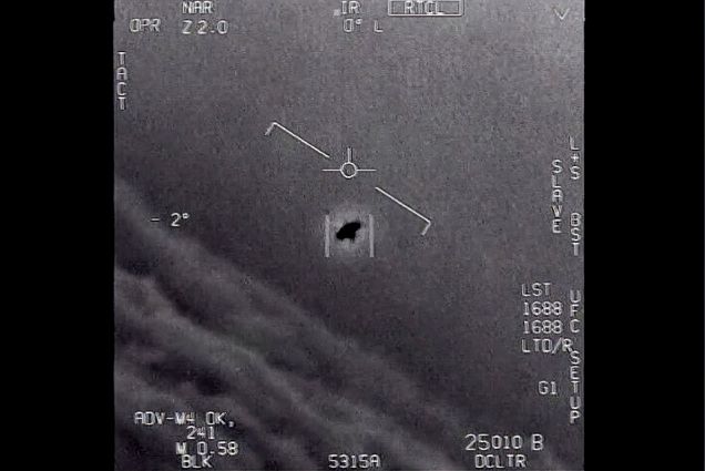 Black and white image from video provided by the Department of Defense labelled Gimbal, from 2015, an unexplained object is seen at center as it is tracked as it soars high along the clouds, traveling against the wind. Numbers in white are seen around the edge of the image.