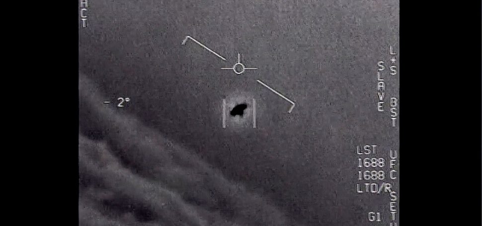 Black and white image from video provided by the Department of Defense labelled Gimbal, from 2015, an unexplained object is seen at center as it is tracked as it soars high along the clouds, traveling against the wind. Numbers in white are seen around the edge of the image.