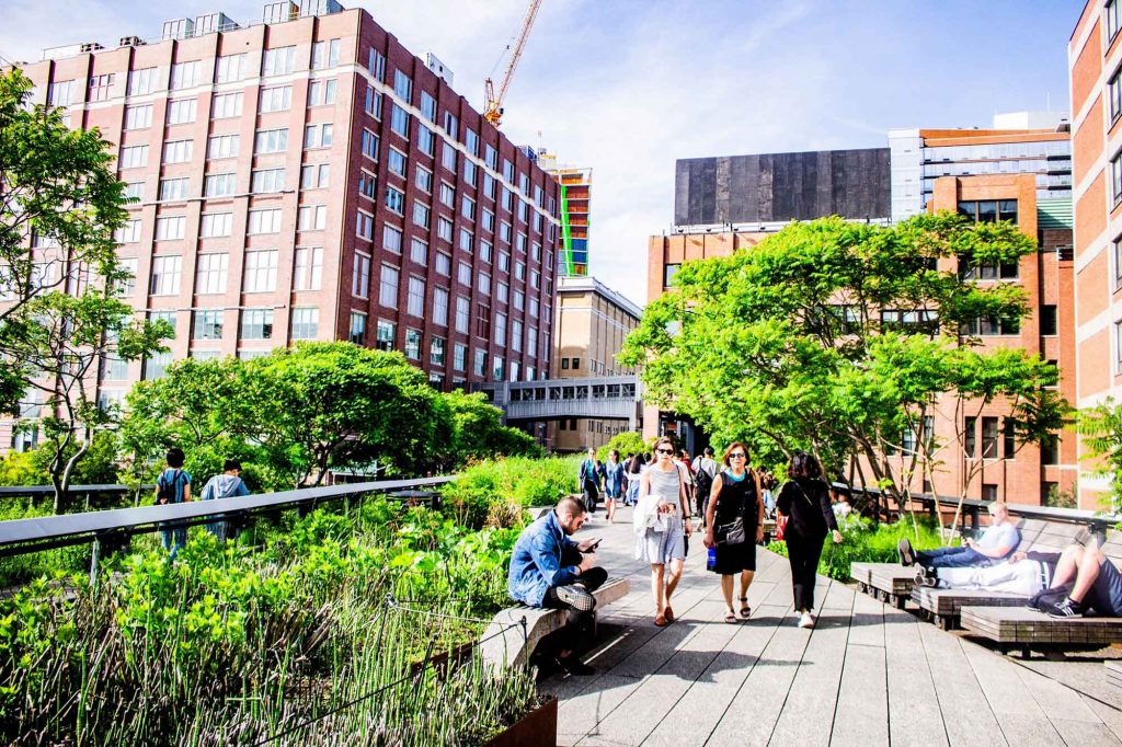 People sit and walk through High Line urban green space park in Manhattan, New York City.