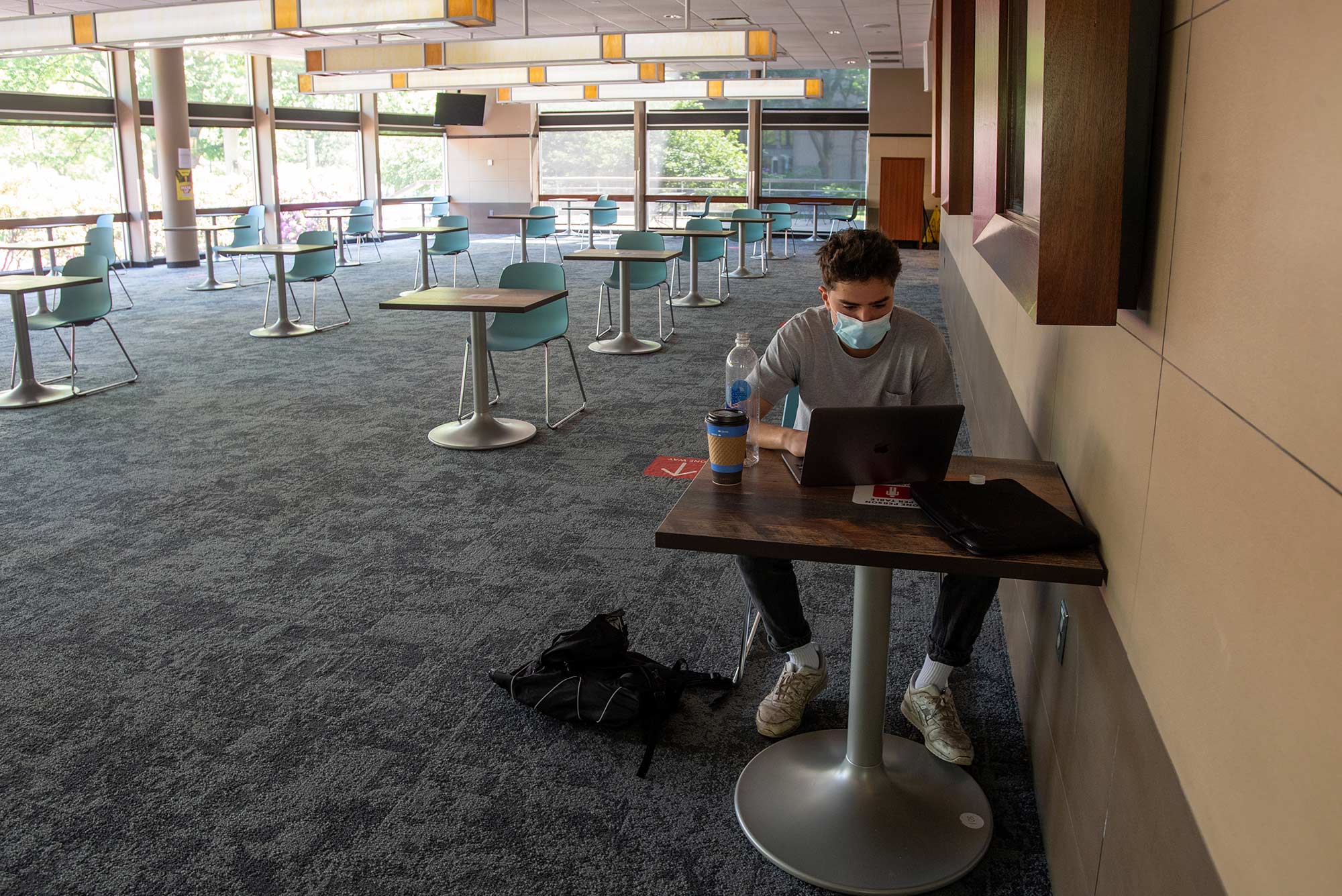 Photo of Jan Block (COM’23), sitting at a social distant desk in the GSU, wearing a face mask and looking at his laptop as he attends his Summer Term 1 global health class virtually from the GSU on May 27.