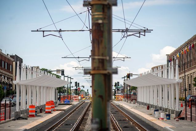 Photo of the new MBTA Amory Street Station taking shape. At the center of the photo is a green, rusted pipe, that is blurred; on either side, are white, shelter structures. The sky is light blue with a few white puffy clouds.