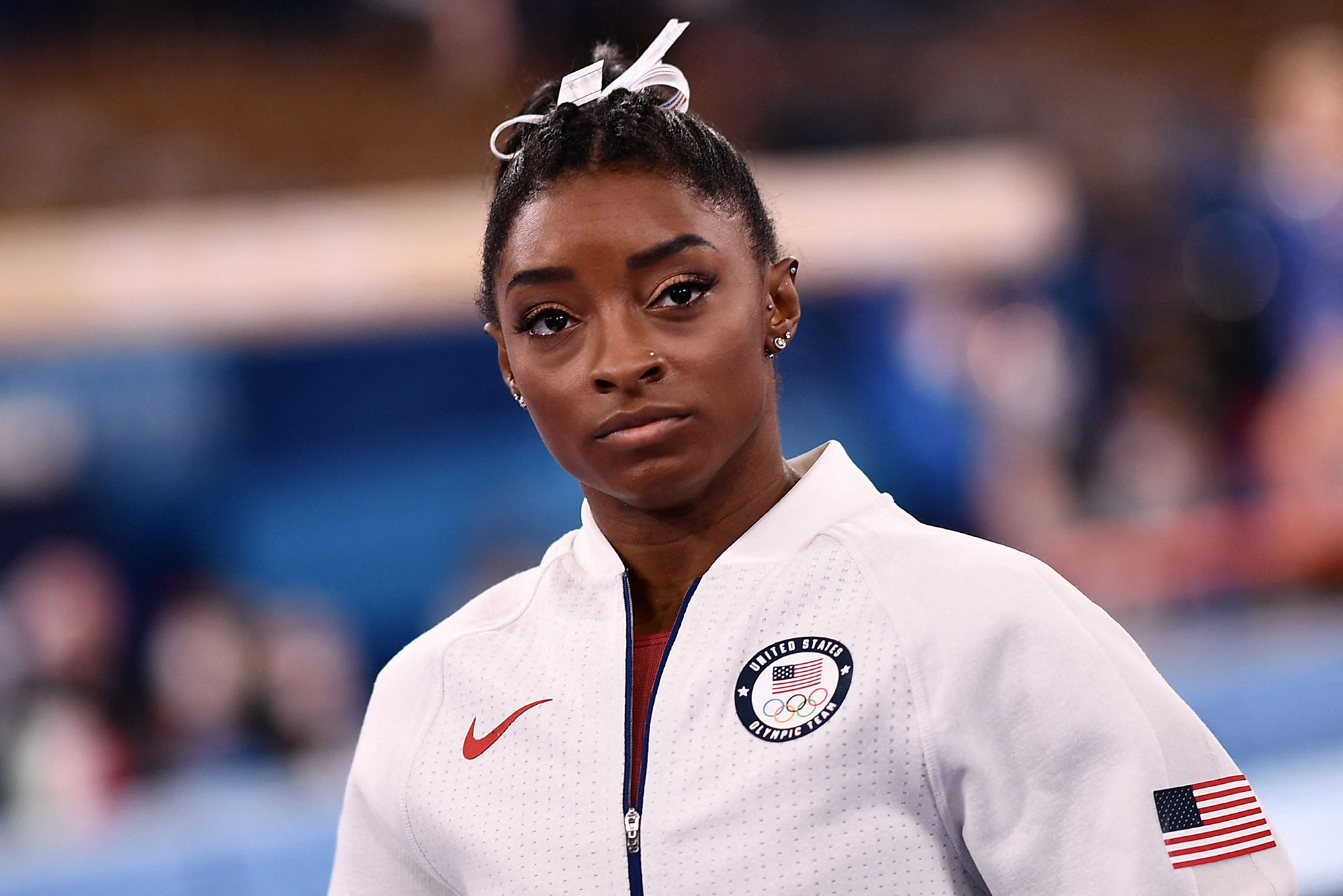 Photo of USA's Simone Biles, in her white USA sweatsuit, looking a little somber as she waits for the final results of the artistic gymnastics women's team final during the Tokyo 2020 Olympic Games at the Ariake Gymnastics Centre in Tokyo on July 27, 2021.