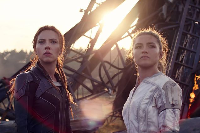 Movie still from Black Widow, starring Scarlett Johannson as Natasha Romanoff/Black Widow, at left, wearing a black leather jacket, next to Florence Pugh playing her little sister, Yelena Belova. Behind them, some rubble is seen in the distance.