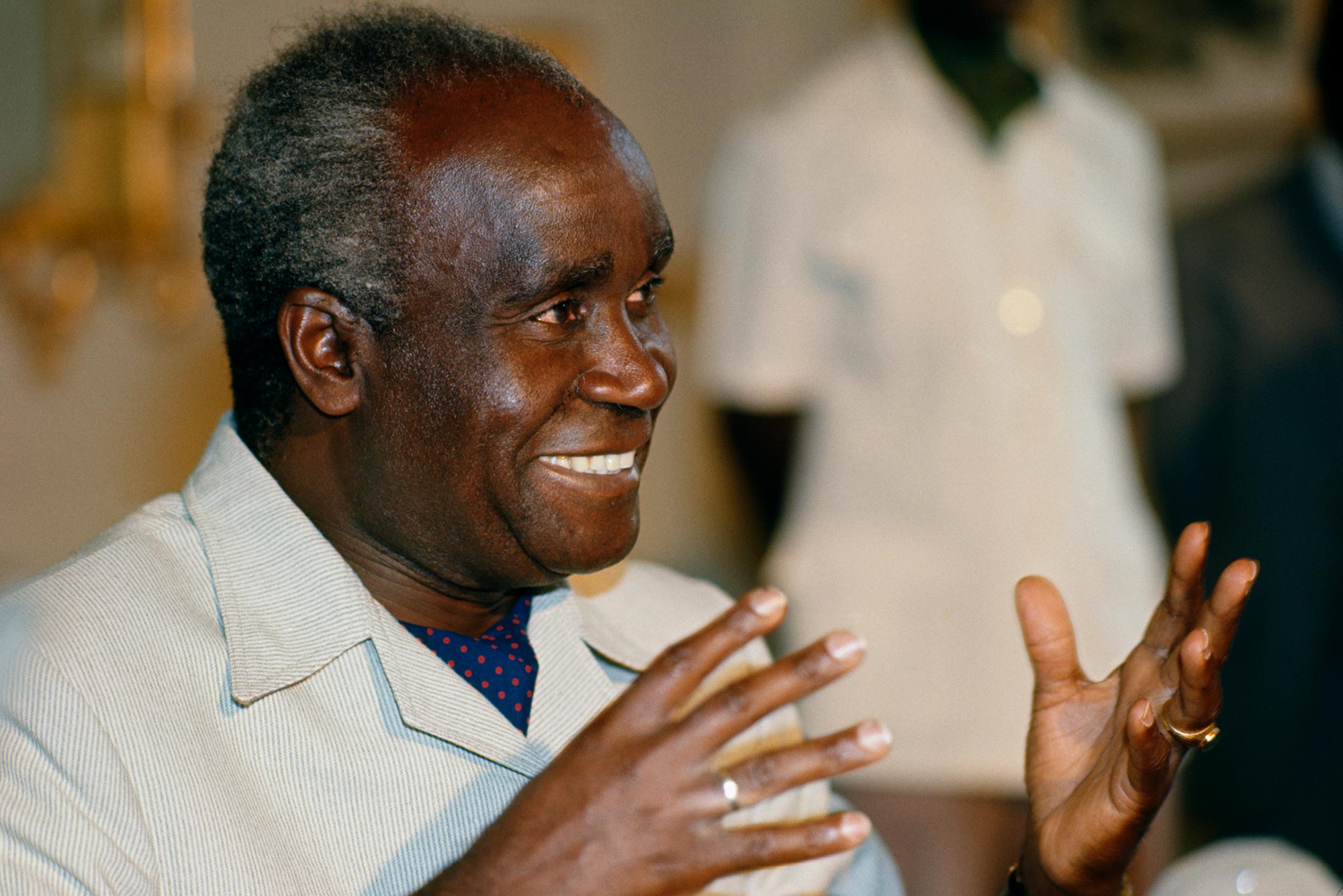 Photo of former President of Zambia, Kenneth Kaunda, smiling and gesturing with his hands. Photo was taken May 24, 1977.