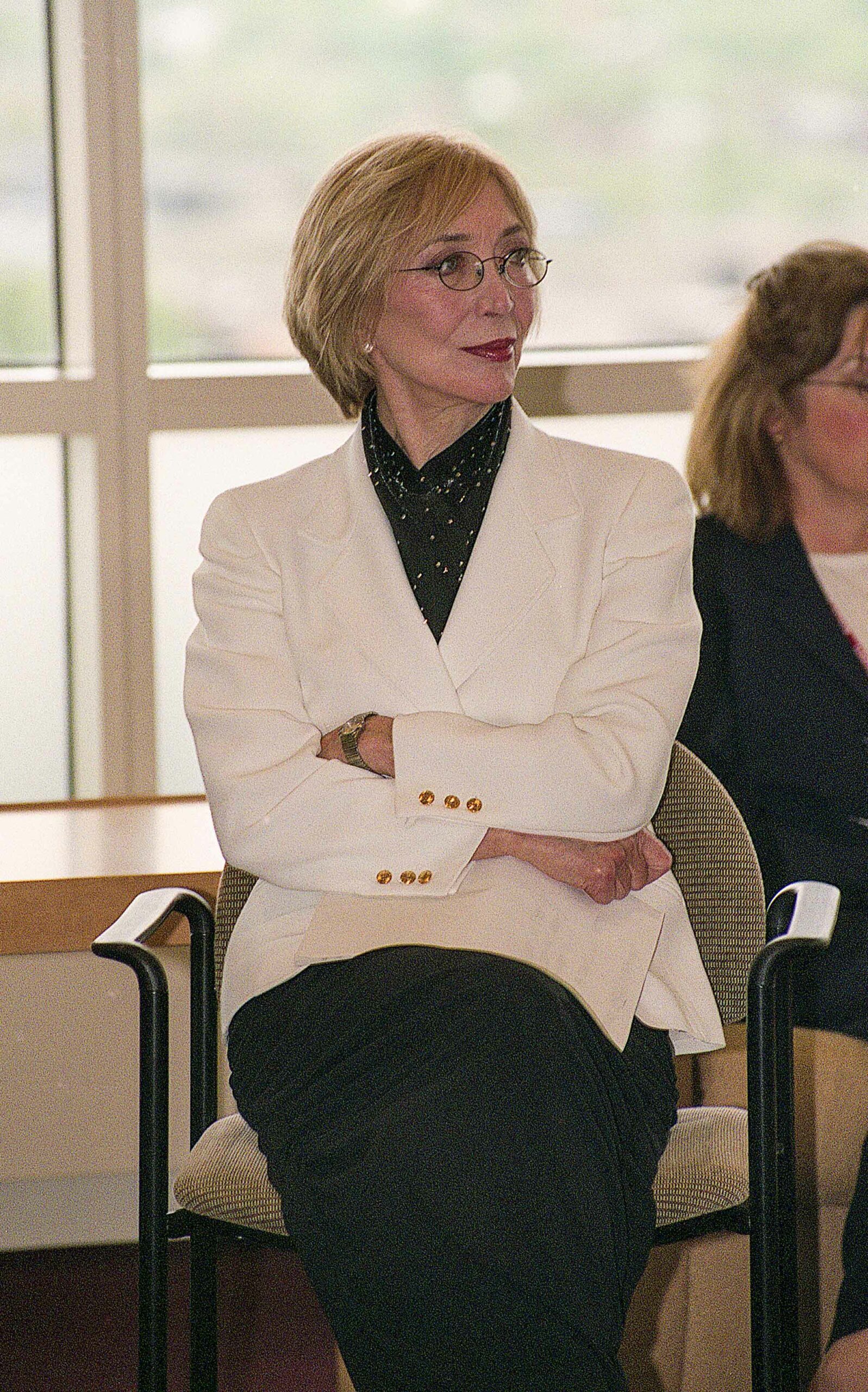 Fashion designer Jessica McClintock sits with arms crossed watching a presentation.