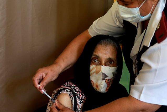 Photo of a seventy six year old woman Kaironesa Sheik Suleman Allie receiving her first dose of the Pfizer COVID-19 vaccine from a health staff member, at a vaccination centre, in Karl Bremer Hospital, in Cape Town, South Africa, Wednesday, May 26, 2021. The staffer wears a blue paper facemask and reaches over her to give the vaccination.