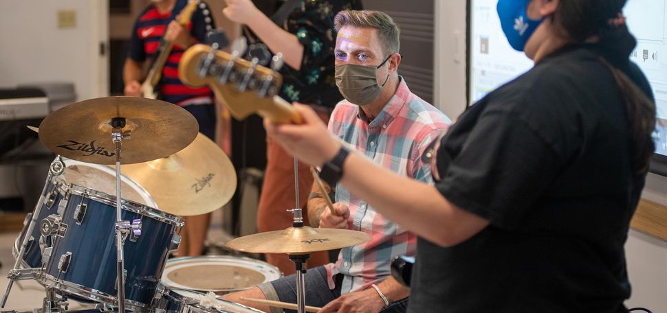 Photo of Paul Halpainy (CFA’19) in rock band performance and pedagogy at CFA August 2. He is seated at the drum, and a person with a black t-shirt plays the bass guitar in the right foreground.