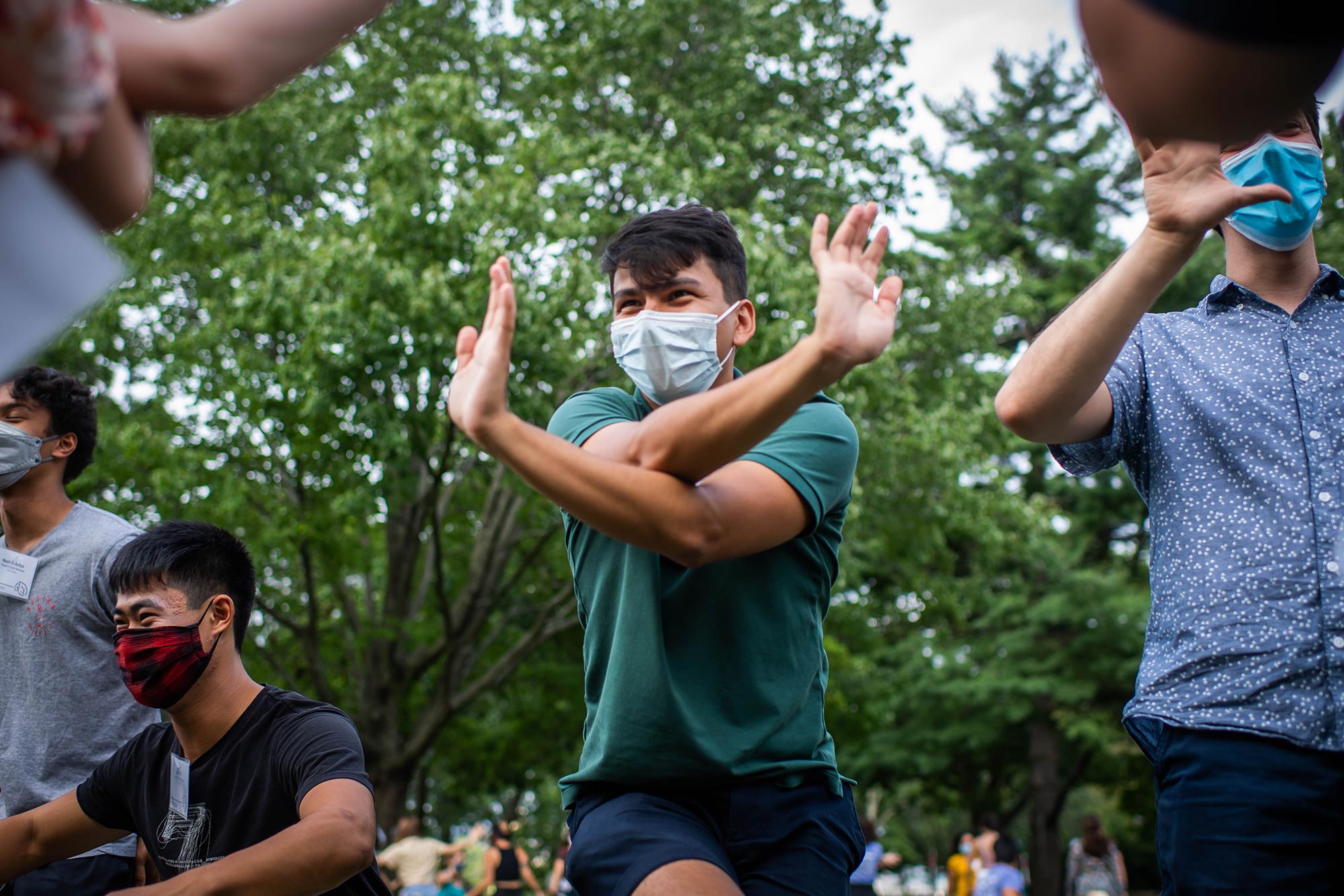 Photo of Giancarlo Sirio (CAS’22), who wears a hunter green shirt and a paper face mask, with his arms crossed, enjoying himself as he participates in a team-building exercise during a FYSOP staff leader training workshop on the BU Beach. Other participants are seen around him.