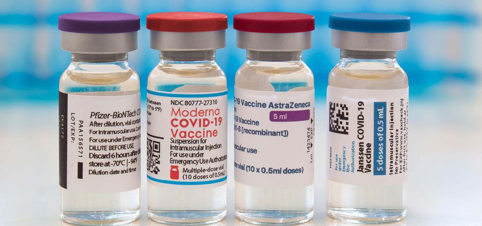 Bottles of the Pfizer, Moderna, AstraZeneca, and Johnson & Johnson COVID-19 vaccines sit on a table next to a syringe.