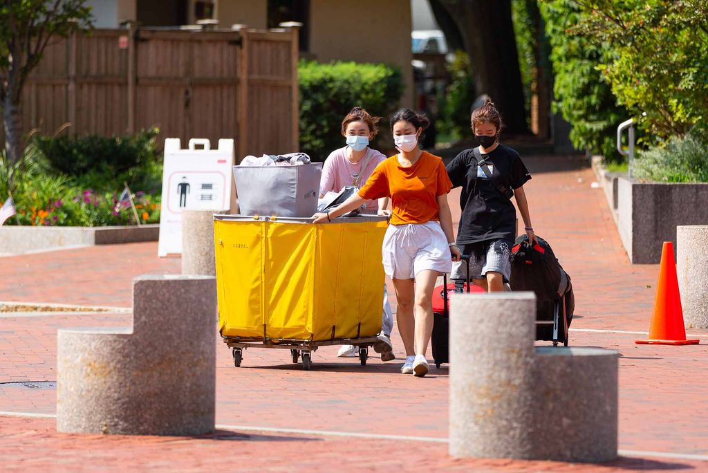 An Asian student and their family pull a yellow moving cart while moving into student dorms for the fall semseter.