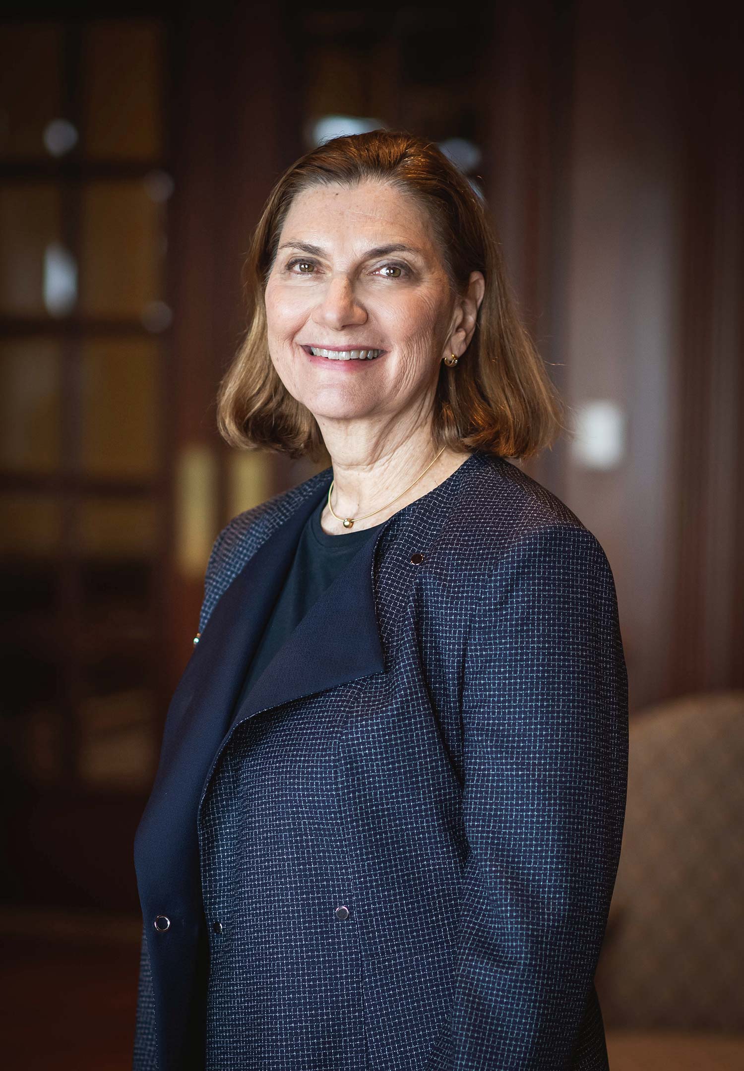 Headshot of Pat O’Brien in a navy blue jacket. A dark wooden-paneled office space is seen behind her.