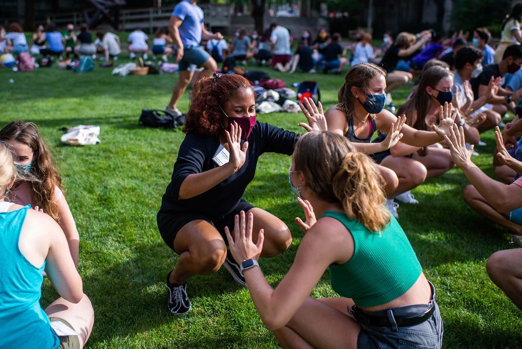 Sarah Lopez (CAS’23), who wears a black and red face mask and a black t-shirt, crouches down and extends her arms as if to ask for a double high-five from another student across from her. Other students are seen participating behind her.