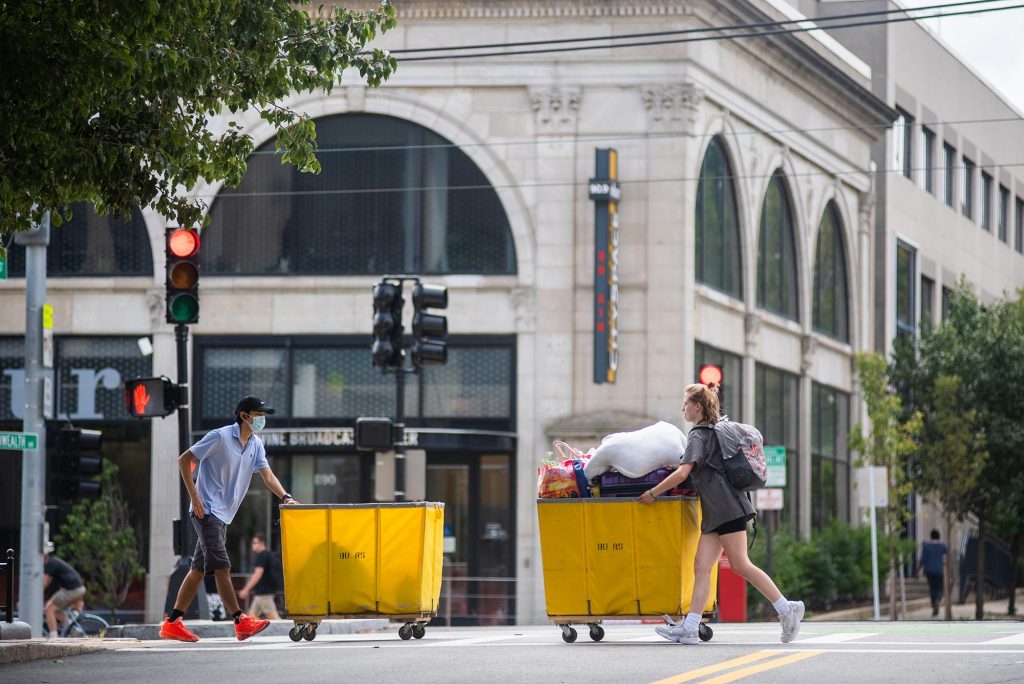 Photo of students rolling bright yellow moving bins in opposite directions along Commonwealth Ave on Transition Day Move in on campus August 16, 2021.