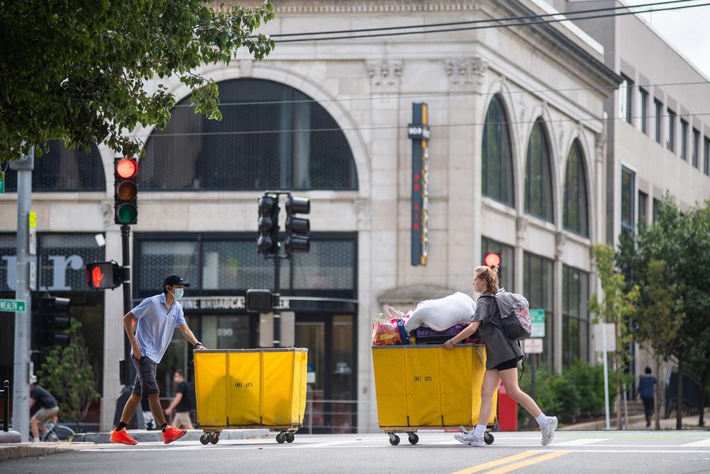 Photo of students rolling bright yellow moving bins in opposite directions along Commonwealth Ave on Transition Day Move in on campus August 16, 2021.