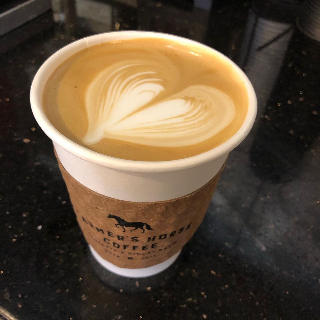 photo of hot latte in white to-go cup with heart-shaped foam art on the top.
