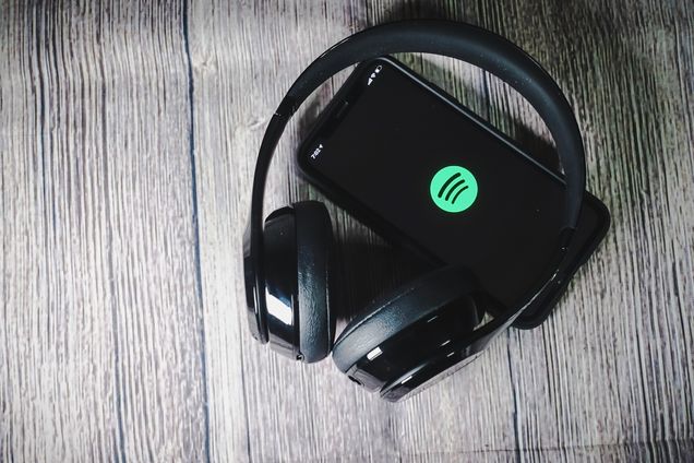 An iphone 11 screen showing spotify icon with Beats headphones lying on a wooden tabletop