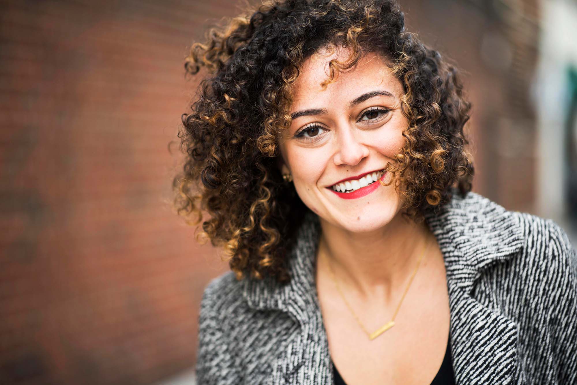 Portrait of Danielle Letayf, founder of the start-up business Badassery, outside with a brick wall in the background.