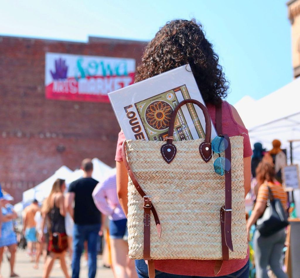 View from behind a woman attending the SoWa Open Market carrying a backpack with a piece of purchased art sticking out of the bag.