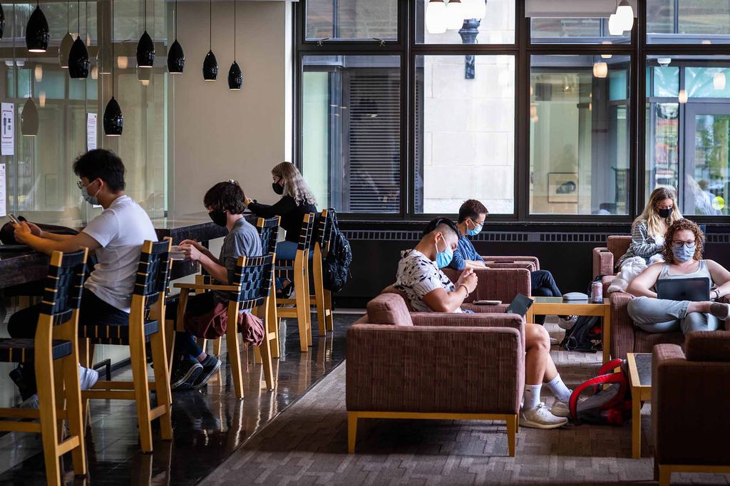 Students wearing protective face coverings sit and study in the lounge of the College of General Studies lobby at Boston University.