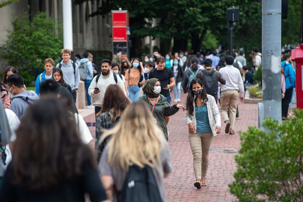 Students walk along the sidewalks of Commonwealth Ave on the Boston University Charles River Campus September 2, 2021. Two women at the center of the crowds are wearing face coverings and talking.