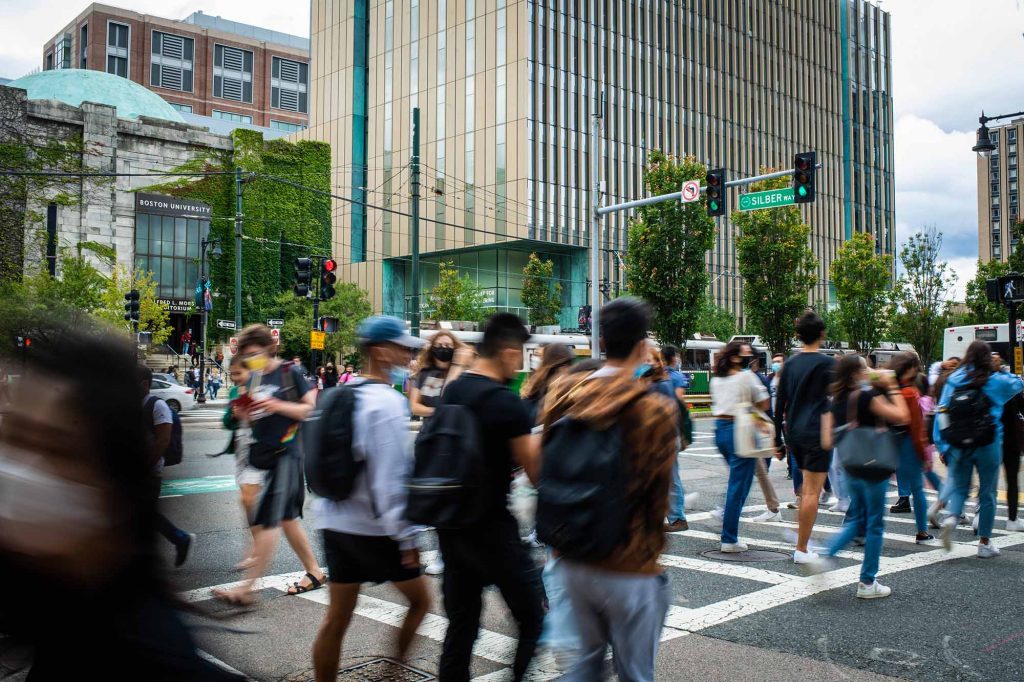 Crowds of students and people cross Commonwealth Ave near the Kilachand Center seen in the background.