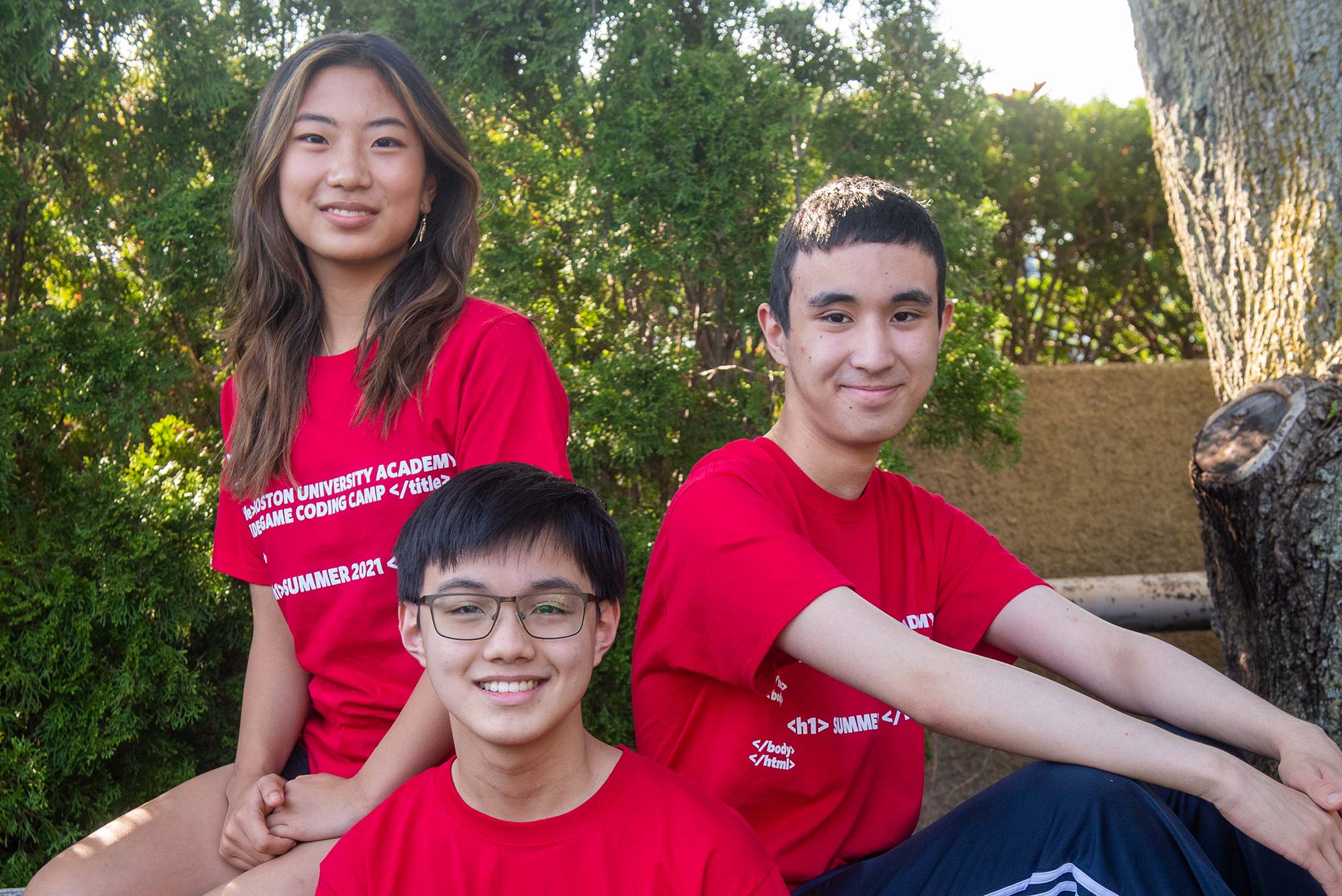 Photos of Joie Liu (from left), Alvin Lu, and Gabriel Romualdo, wearing read shirts and smiling as they sit on the edge of a park bench. Trees are seen behind them.