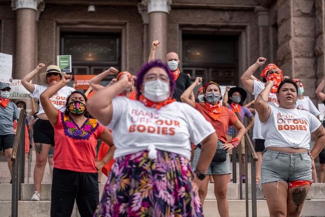 Photo of Pro-choice protesters perform outside the Texas State Capitol on Wednesday, Sept. 1, 2021 in Austin, TX. The protesters raise their fists and wear shirts that say "BANS OFF OUR BODIES"