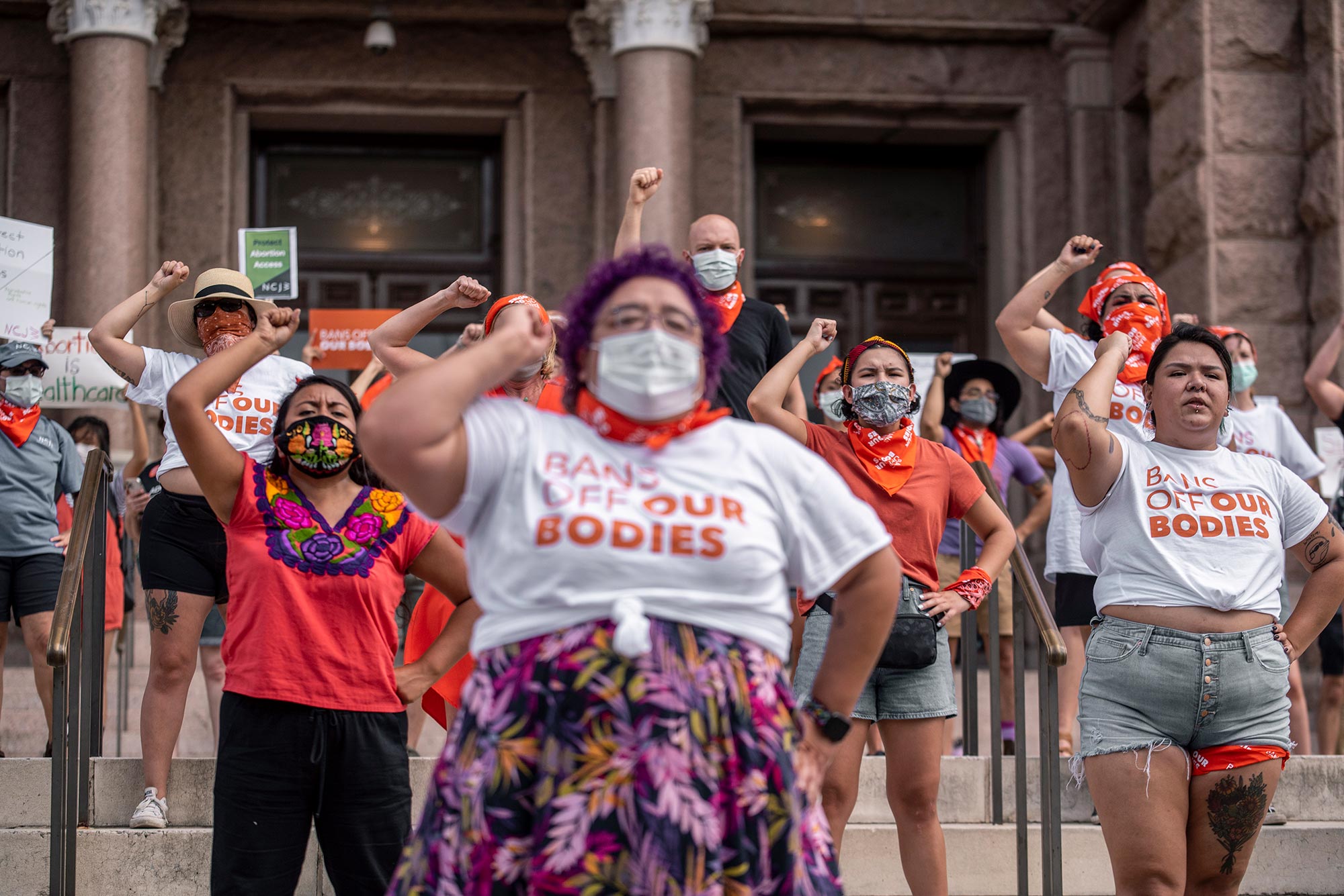 Photo of Pro-choice protesters perform outside the Texas State Capitol on Wednesday, Sept. 1, 2021 in Austin, TX. The protesters raise their fists and wear shirts that say "BANS OFF OUR BODIES"